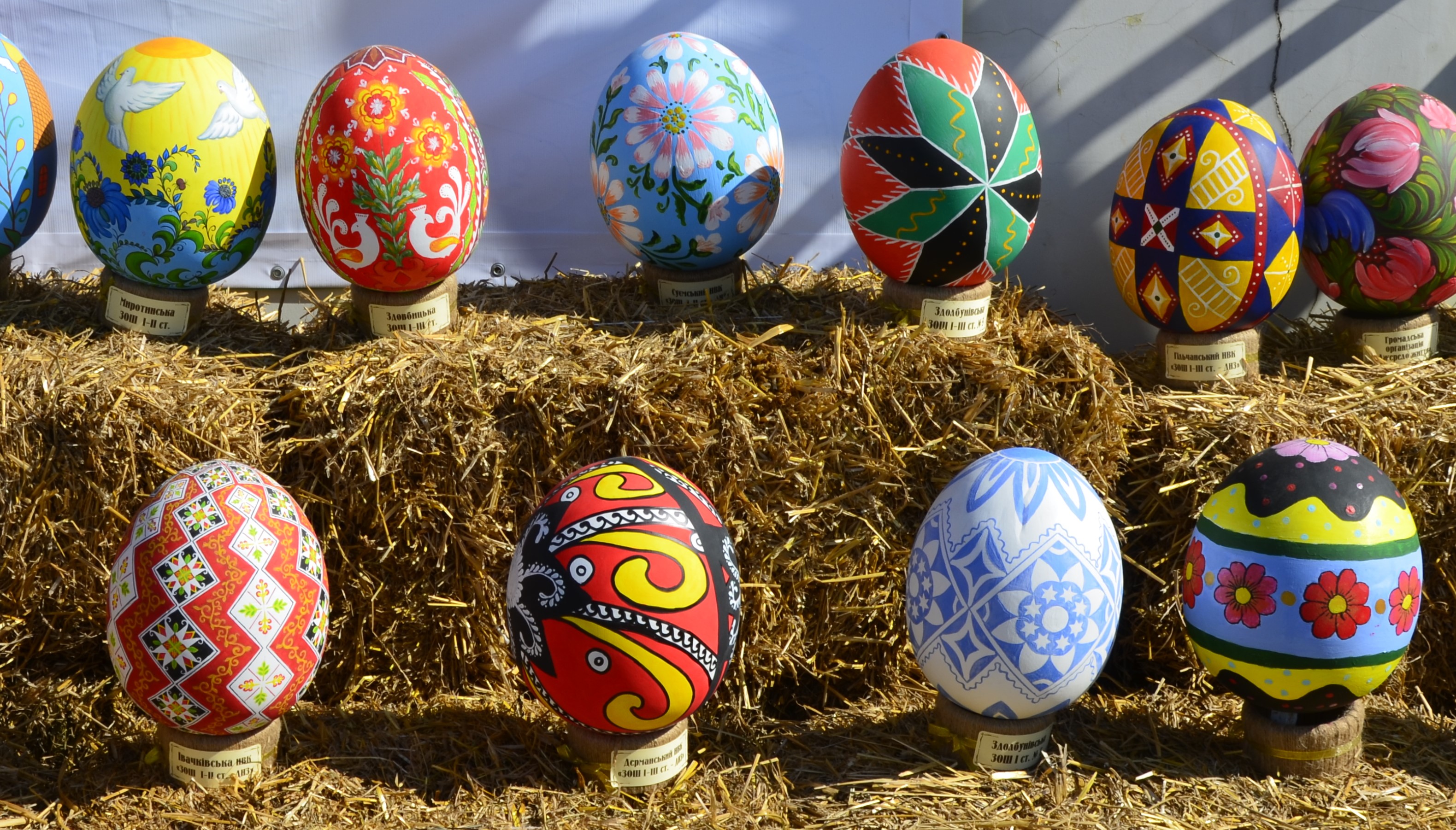 colourful painted eggs on stands resting on some hay